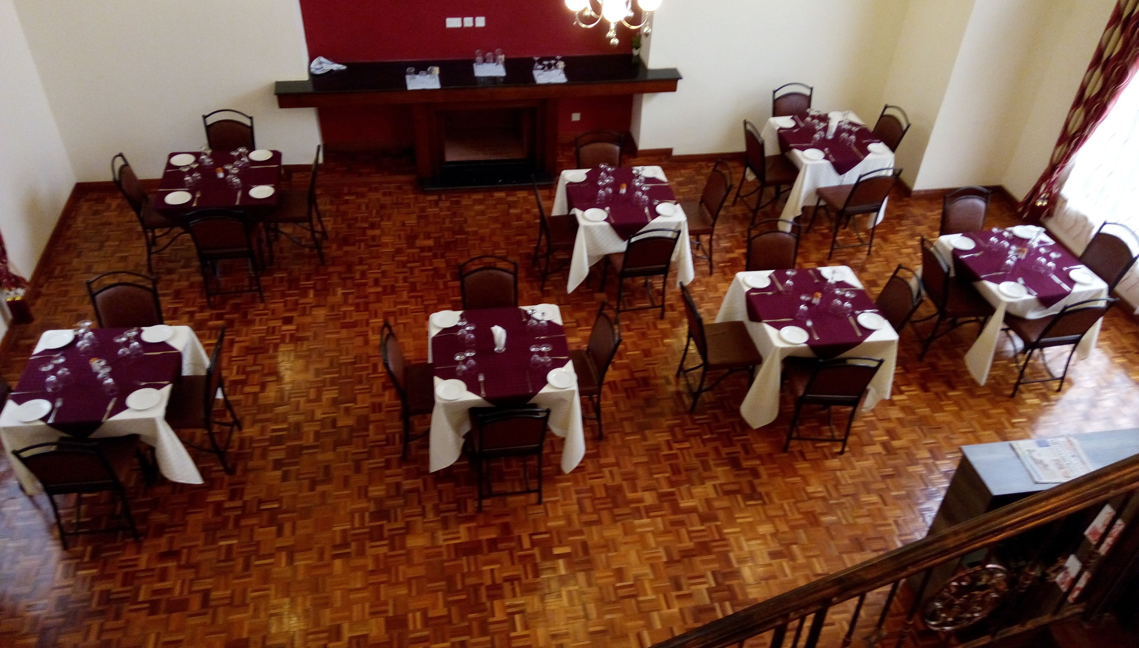 Un comedor con varias mesas dispuestas para comidas, suelo de madera y una chimenea al fondo.