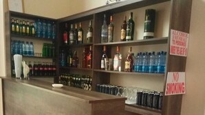 Zona de bar con estantes llenos de botellas y vasos. Se observan carteles que indican la prohibición de fumar y la restricción de venta de alcohol a menores.
