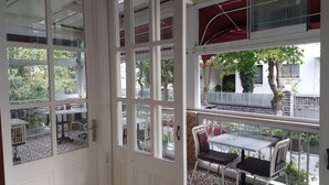 A room with a large glass door leading to an outdoor area with a table and chairs, a view of trees and a fence, and a balcony with a railing. - Yeşilköy Airport Butik Otel (Istanbul)