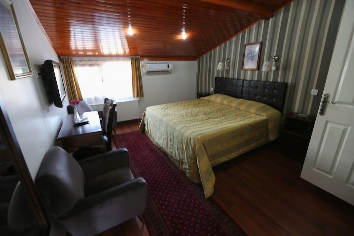 A bedroom with a bed, a desk, a chair, and a window with curtains.