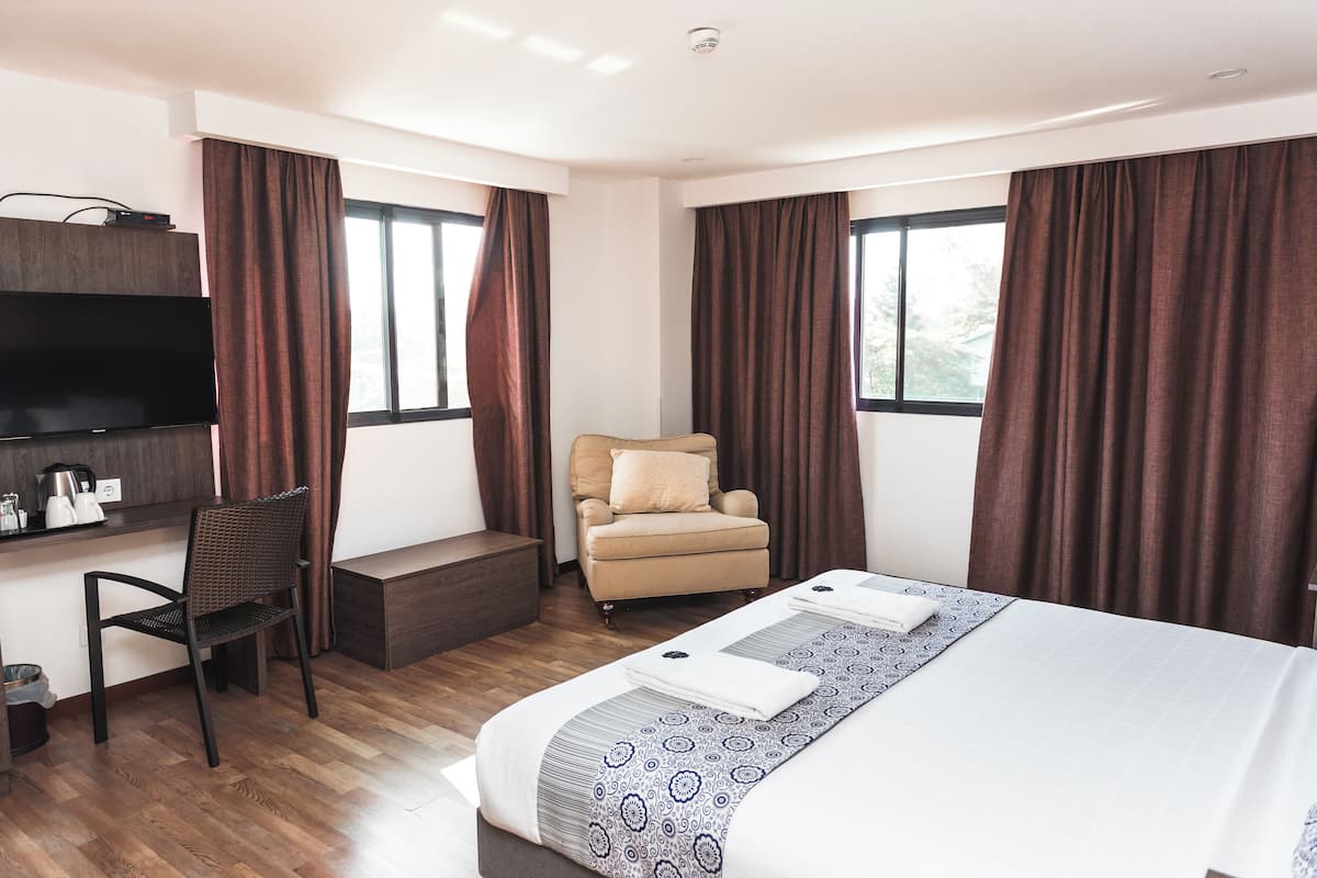 A hotel room with a bed, a desk with a TV, a chair, and large windows with curtains.