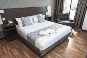 A neatly made bed with patterned bedding, a bedside phone, a chair, and a nightstand with a lamp.