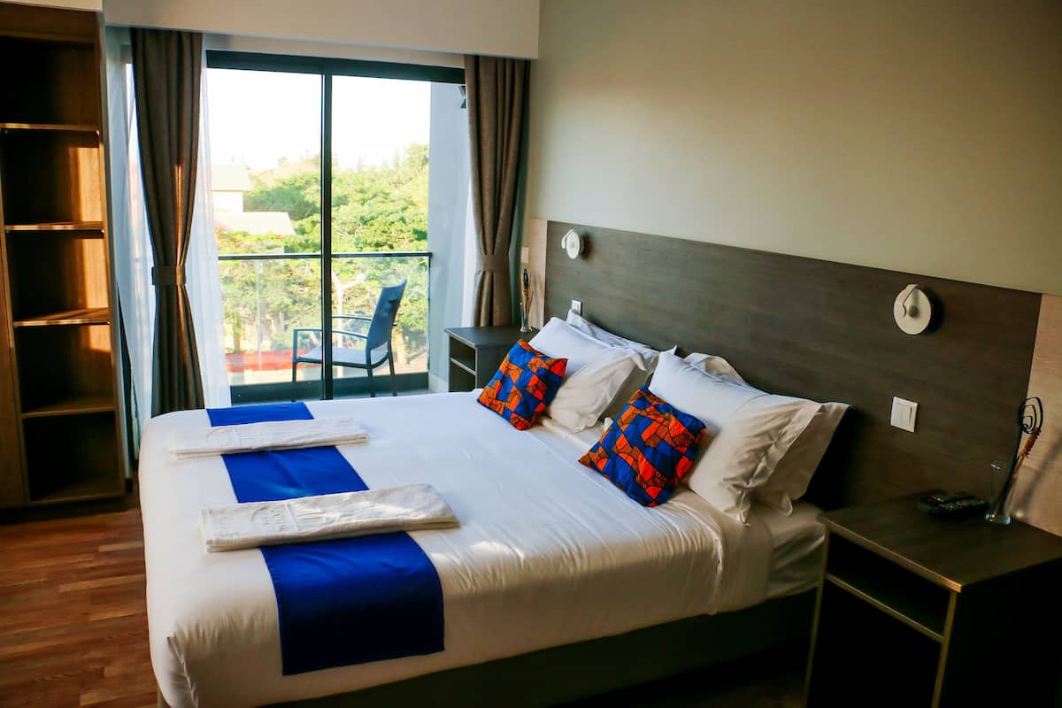 A hotel room with a large bed, a nightstand, a chair, and a view of greenery outside.