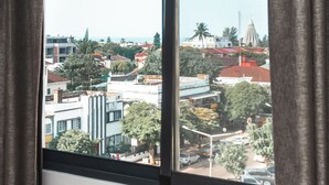 A view from a window with curtains, overlooking a cityscape with buildings, trees, and a distant tower. - Hotel Kapital (Maputo)