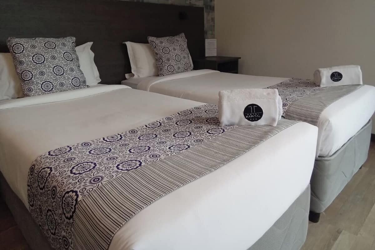 A hotel room with two beds, each with patterned bedspreads and pillows, a headboard, and a nightstand.