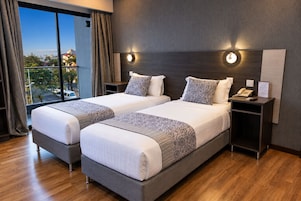 Habitación de hotel con dos camas, una mesita de noche con teléfono y vista a la ciudad.