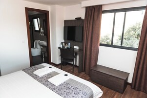 Una habitación de hotel con cama, escritorio, televisor y ventana con cortinas.