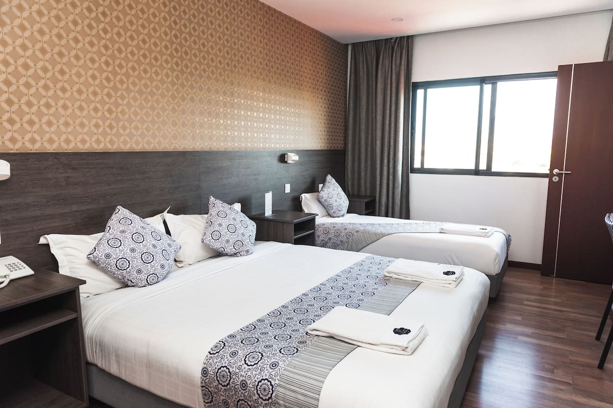A hotel room with two beds, a nightstand with a phone, a headboard, and a window with curtains.