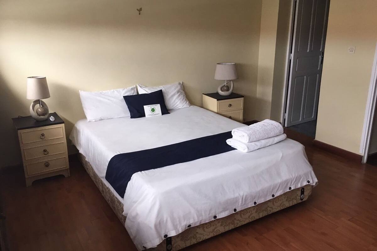 A neatly made bed with white and navy bedding, two bedside tables with lamps, and a wooden floor.