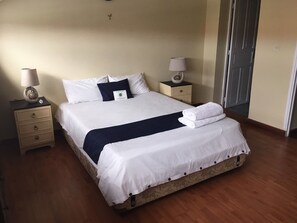 A neatly made bed with white and navy bedding, two bedside tables with lamps, and a wooden floor.