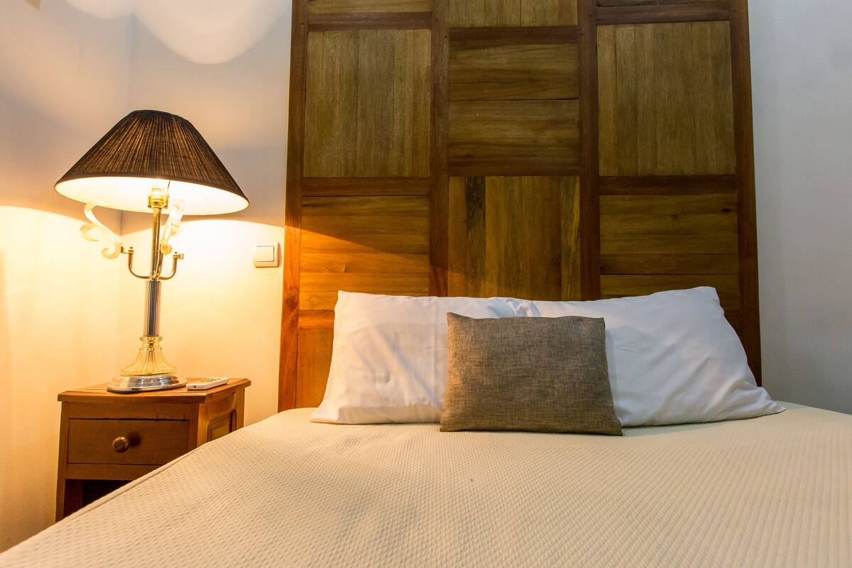 A neatly made bed with white and brown pillows, a wooden headboard, and a bedside table with a lamp.