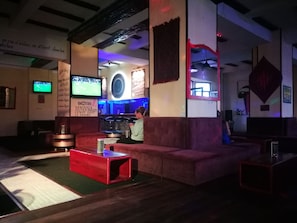 A bar area with a red table, cushioned seating, and a television screen.