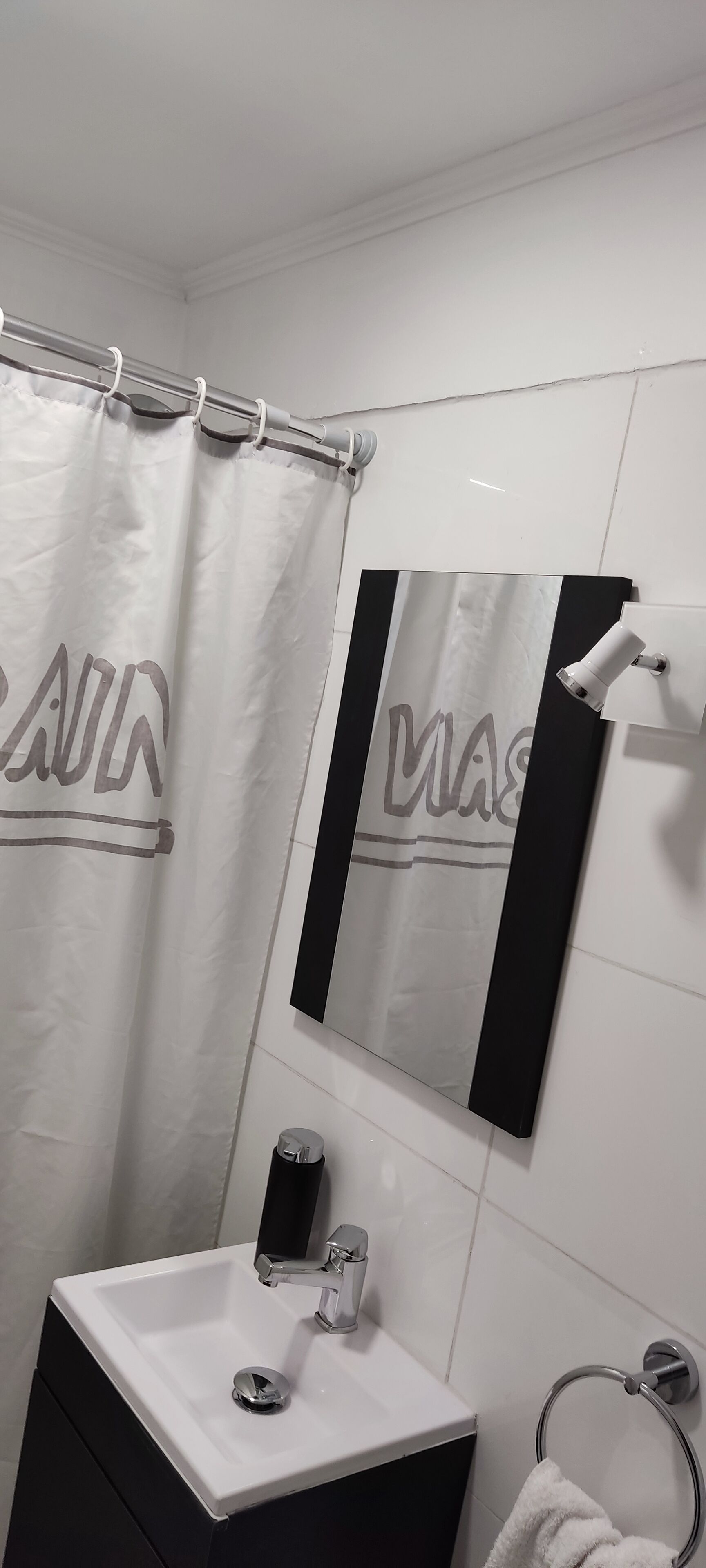 Ein Badezimmer mit einem weißen Waschbecken, einem Spiegel, einem Handtuchhalter und einer Duschvorhang.