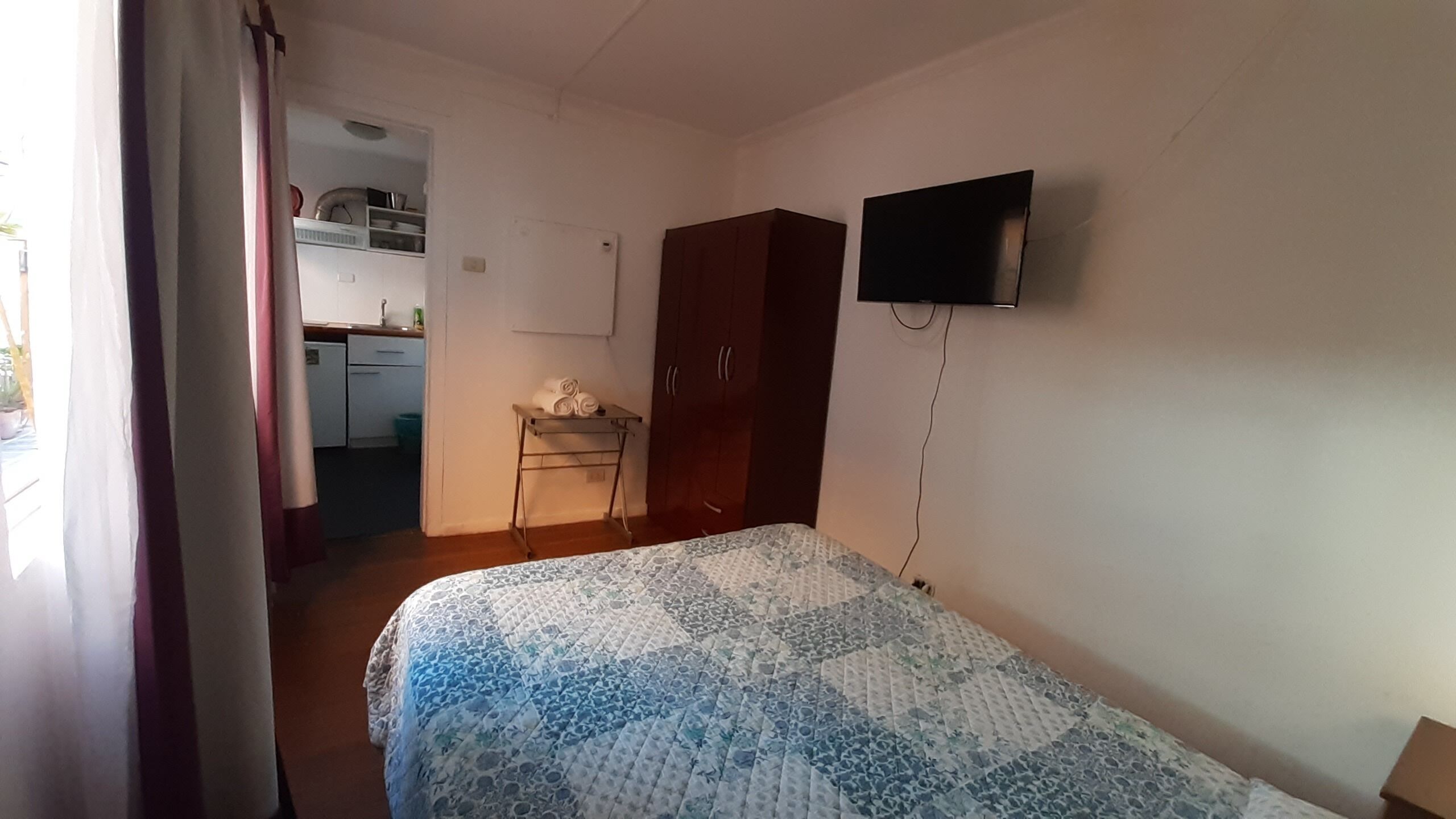 Een slaapkamer met een bed, een aan de muur bevestigde televisie, een garderobe en een klein tafeltje met handdoeken.