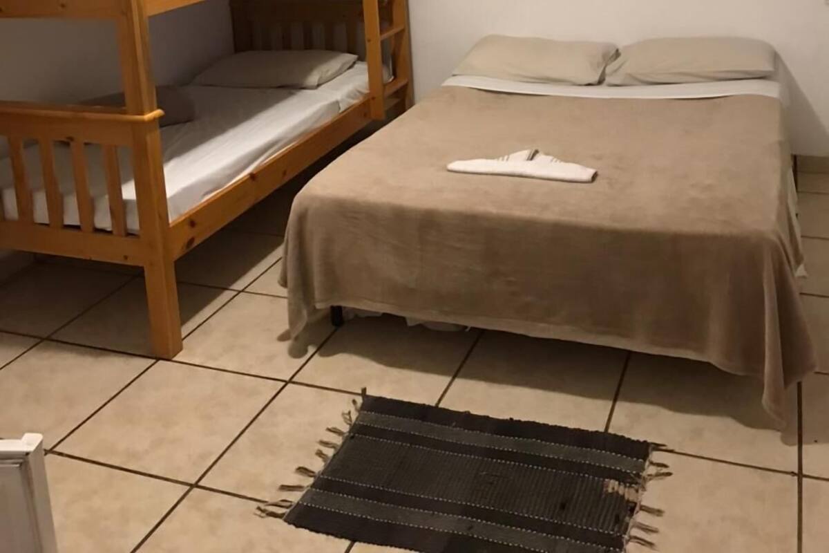 A dormitory room with a bunk bed and a single bed, both with plain bedding. There are two small wall art pieces and a black rug on the floor.
