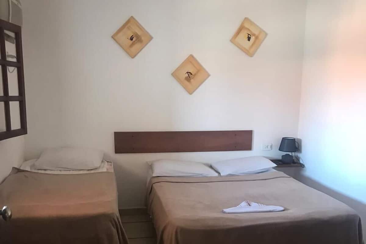 A hotel room with two beds, a wooden headboard, a nightstand with a lamp, and three wall-mounted light fixtures.