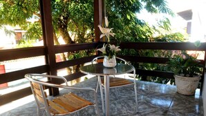 A balcony with a round table and two chairs, a potted plant, and a view of trees and buildings. - Pousada do Marinho (Búzios)