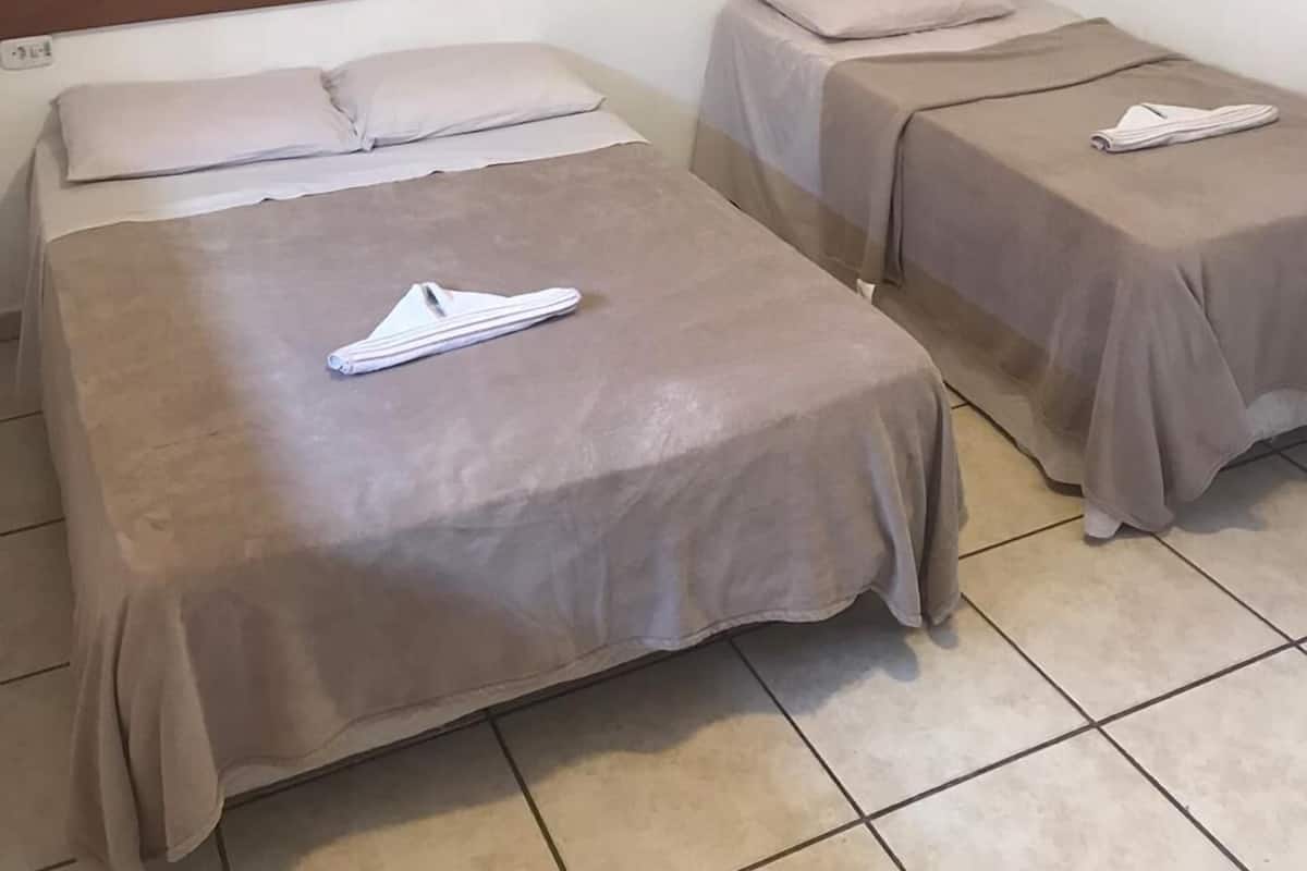 A hotel room with two beds, each with a pillow and a folded towel. There are three red wall decorations above the beds.