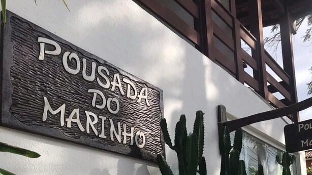 A sign reading "Pousada do Marinho" on a white wall, with cacti and a wooden structure nearby. - Pousada do Marinho (Búzios)
