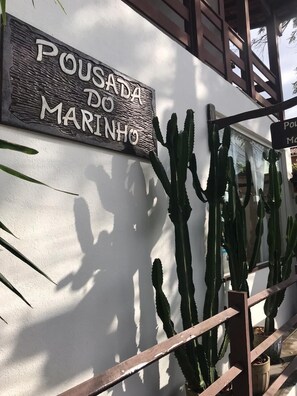 A sign reading "Pousada do Marinho" on a white wall, with cacti and a wooden structure nearby. - Pousada do Marinho (Búzios)