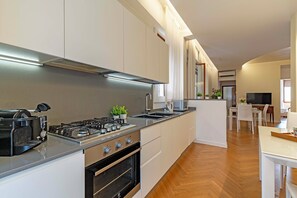 Una cocina moderna con estufa a gas, horno y encimeras de acero inoxidable. Se ve un comedor con una mesa y sillas al fondo.
