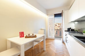 Une cuisine moderne avec des meubles blancs, un coin repas comprenant une table et des chaises blanches, et une vue sur l’extérieur grâce à une porte vitrée.