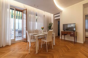 A modern dining area with a wooden herringbone floor, white furniture, and a television on a wooden stand. - Luxury Apartment On Grand Canal by Wonderful Italy (Venice)