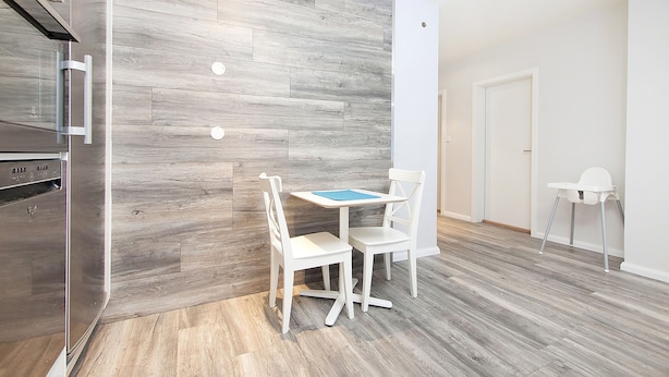 Een moderne keuken met een inbouwoven, een eethoek met tafel en stoelen, en een witte stoel in de hoek.