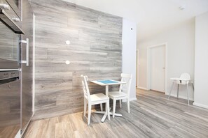 A modern kitchen with a built-in oven, a dining area with a table and chairs, and a white chair in the corner. - Nordurey Guesthouse (Reykjavik)