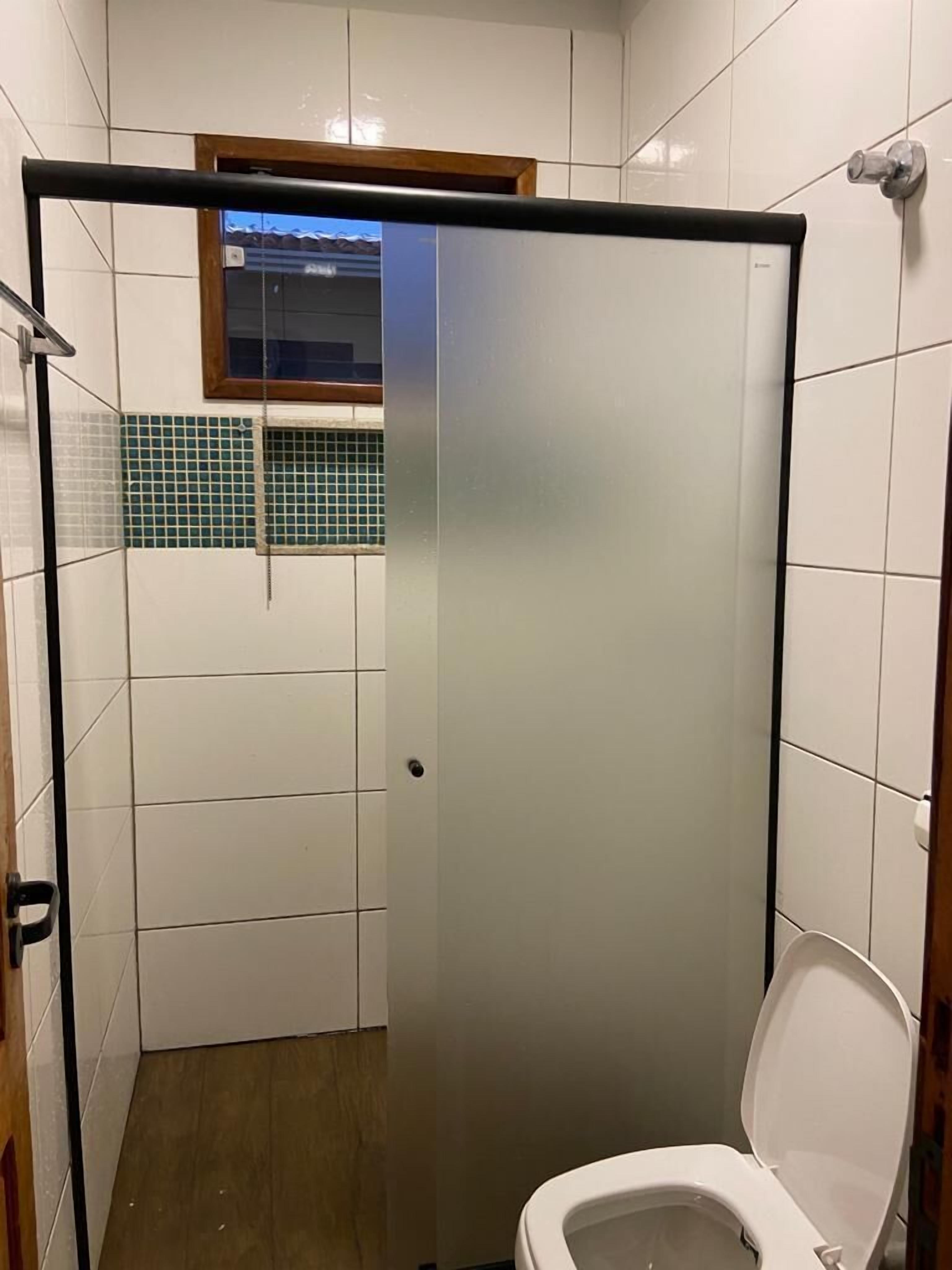 A small, enclosed shower area with a toilet, tiled walls, and a window above the shower.