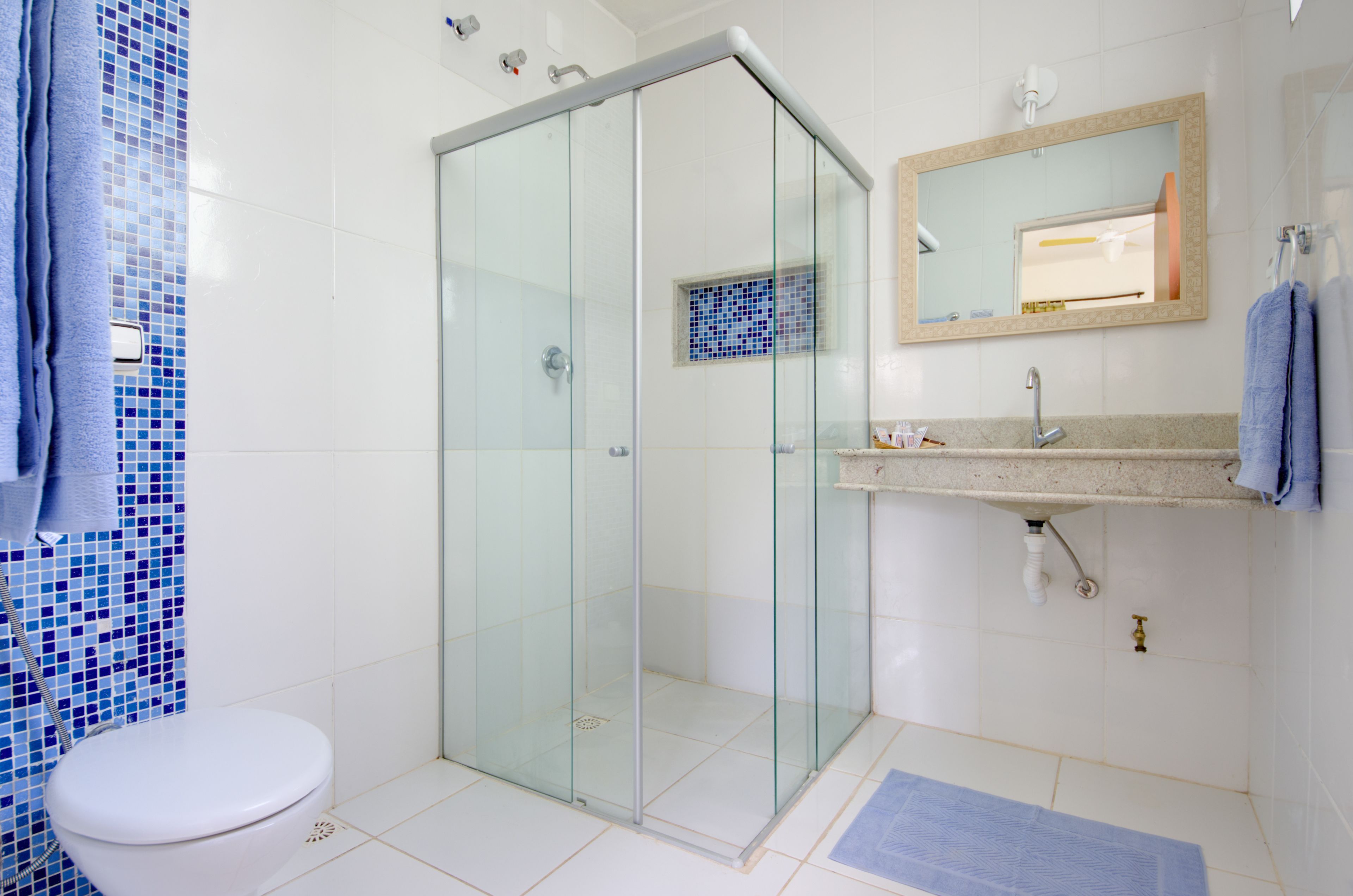 A modern bathroom with a glass-enclosed shower, a white toilet, and a sink with a mirror above it.
