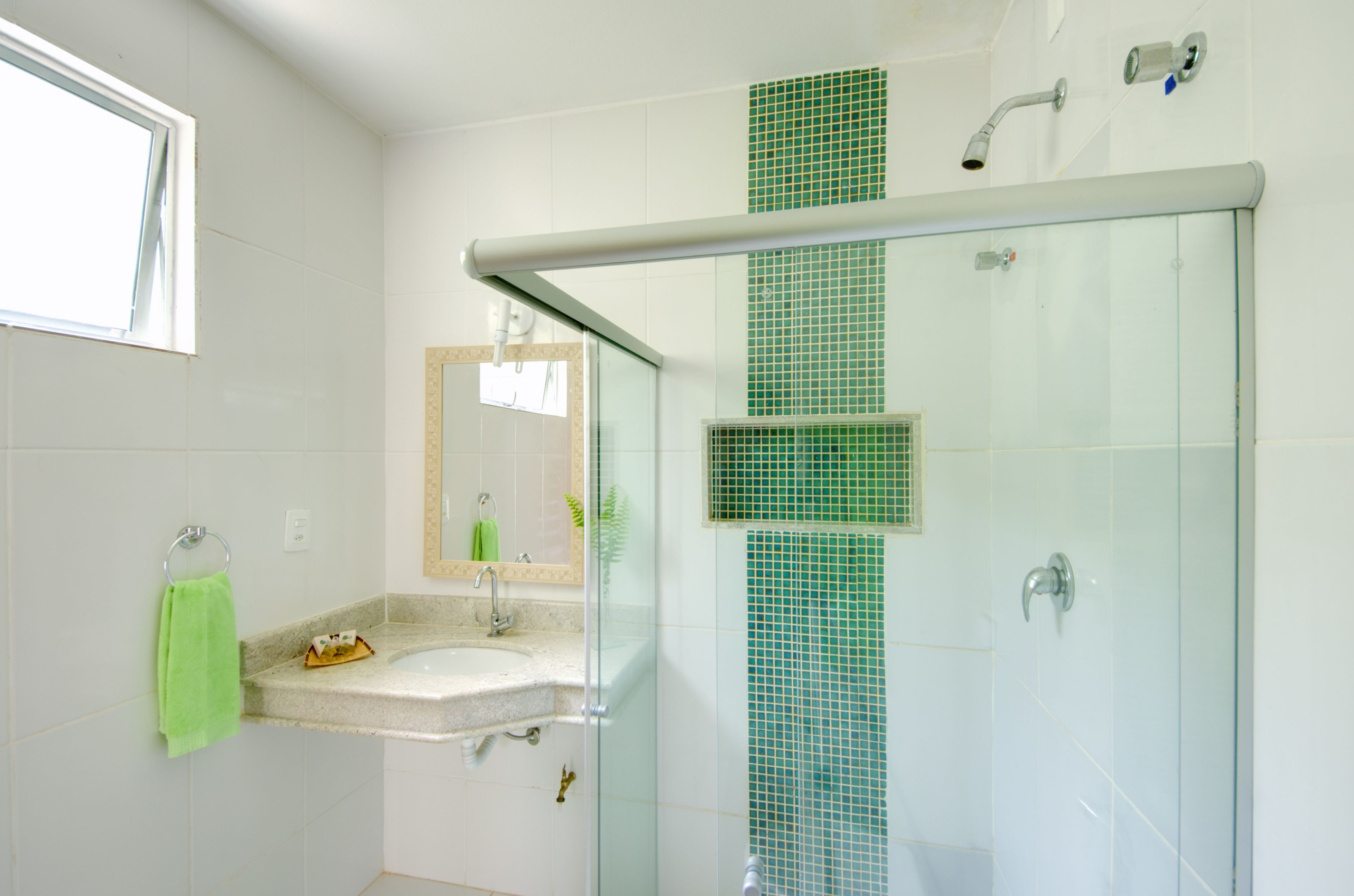 A bathroom with a glass shower enclosure, a sink with a green towel, and a mirror.