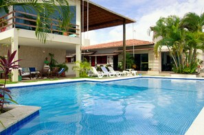 A modern hotel with a swimming pool, lounge chairs, and tropical plants.