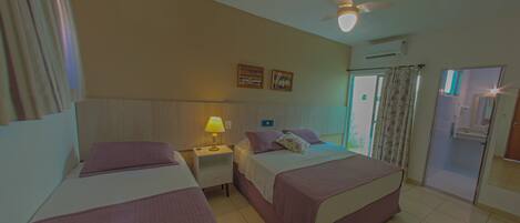 A hotel room with two beds, a ceiling fan, a nightstand with a lamp, and a bathroom visible through an open door.