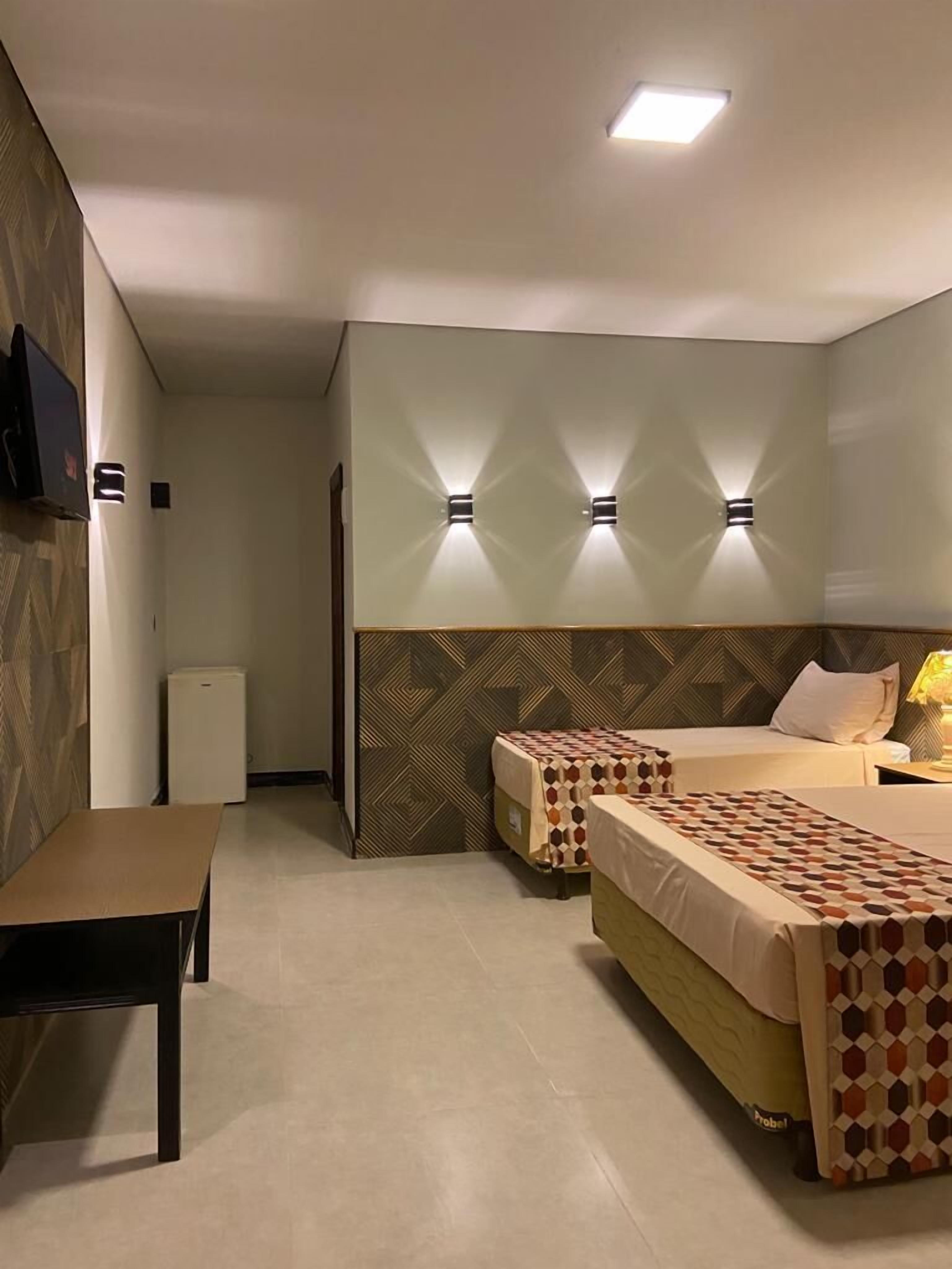 A hotel room with two beds, a desk, and a TV.