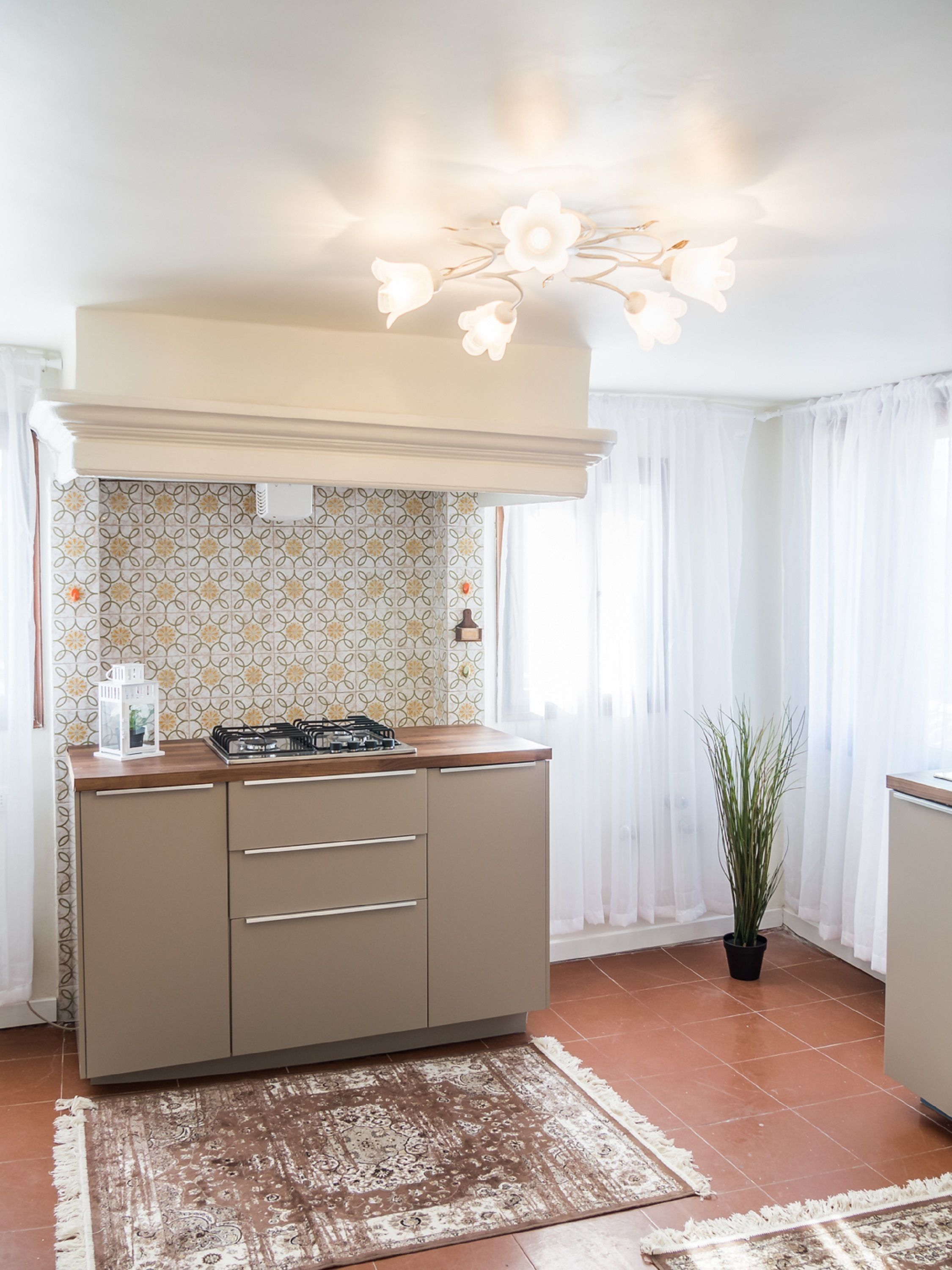 A compact kitchen with a gas stove, beige cabinets, patterned backsplash, and a ceiling light fixture.