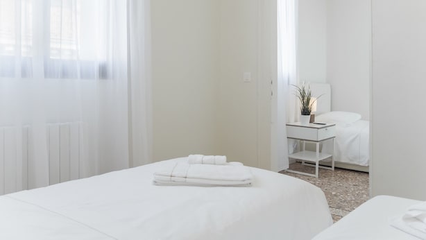 Una camera d'albergo con due letti, un comodino con una lampada e vista attraverso una porta.