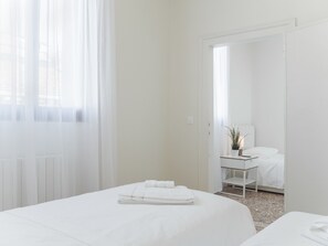 Habitación de hotel con dos camas, una mesita de noche con lámpara y vistas a través de una puerta.