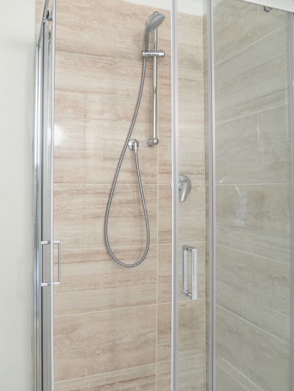 Ducha con cabezal de ducha manual y manguera flexible, frente a una pared de azulejos.