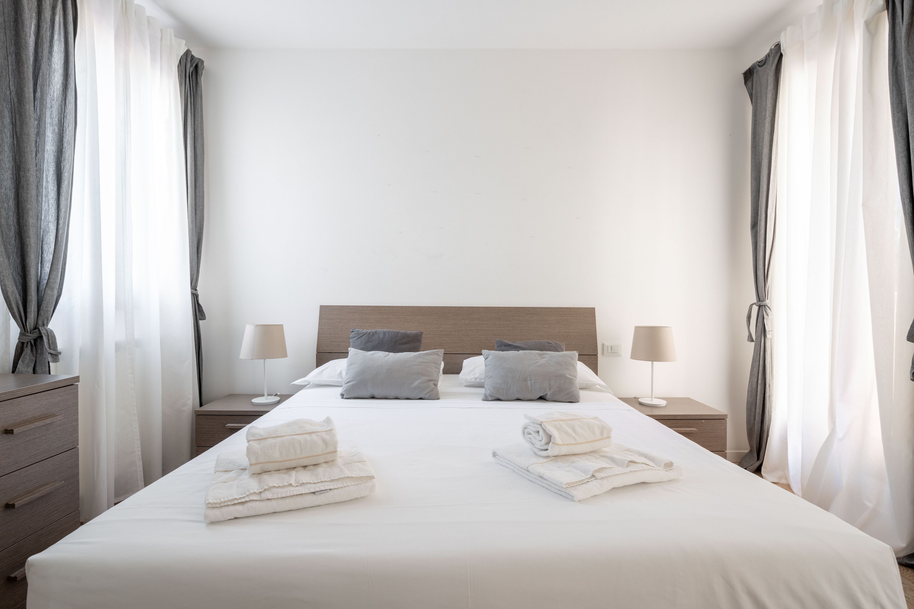 A hotel room with a large bed, two bedside tables with lamps, a wooden headboard, and a view of the city.
