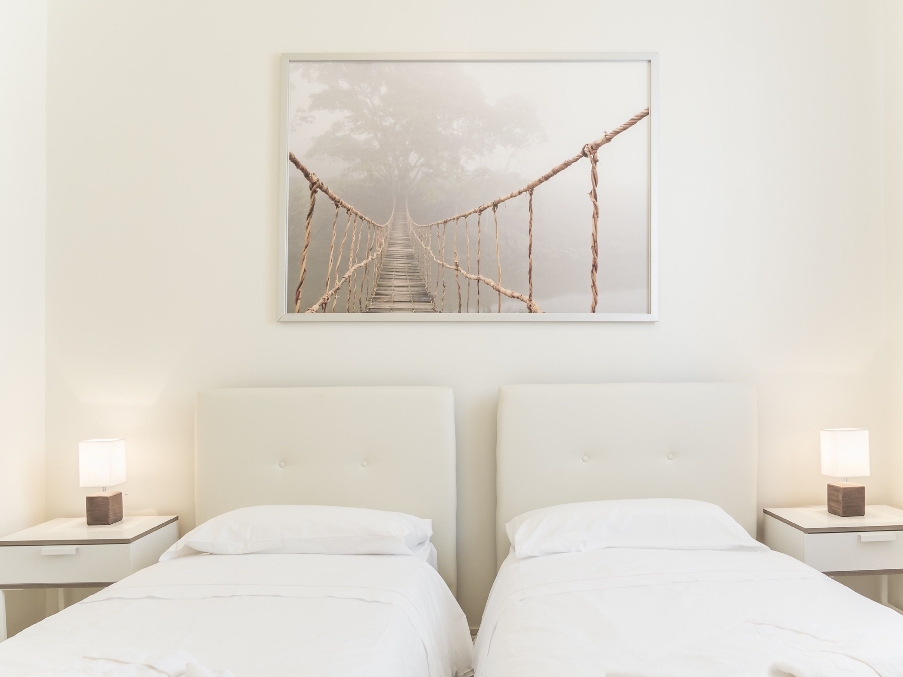 Une chambre d’hôtel avec deux lits, un tableau représentant un pont de corde et des lampes de chevet.