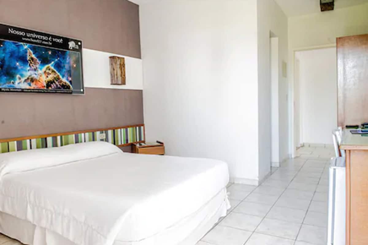 A hotel room with a large bed, a small bedside table, a wall-mounted TV, and a door leading to another room.