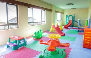 Un área de juegos infantiles con alfombras de colores, un tobogán y estructuras recreativas.