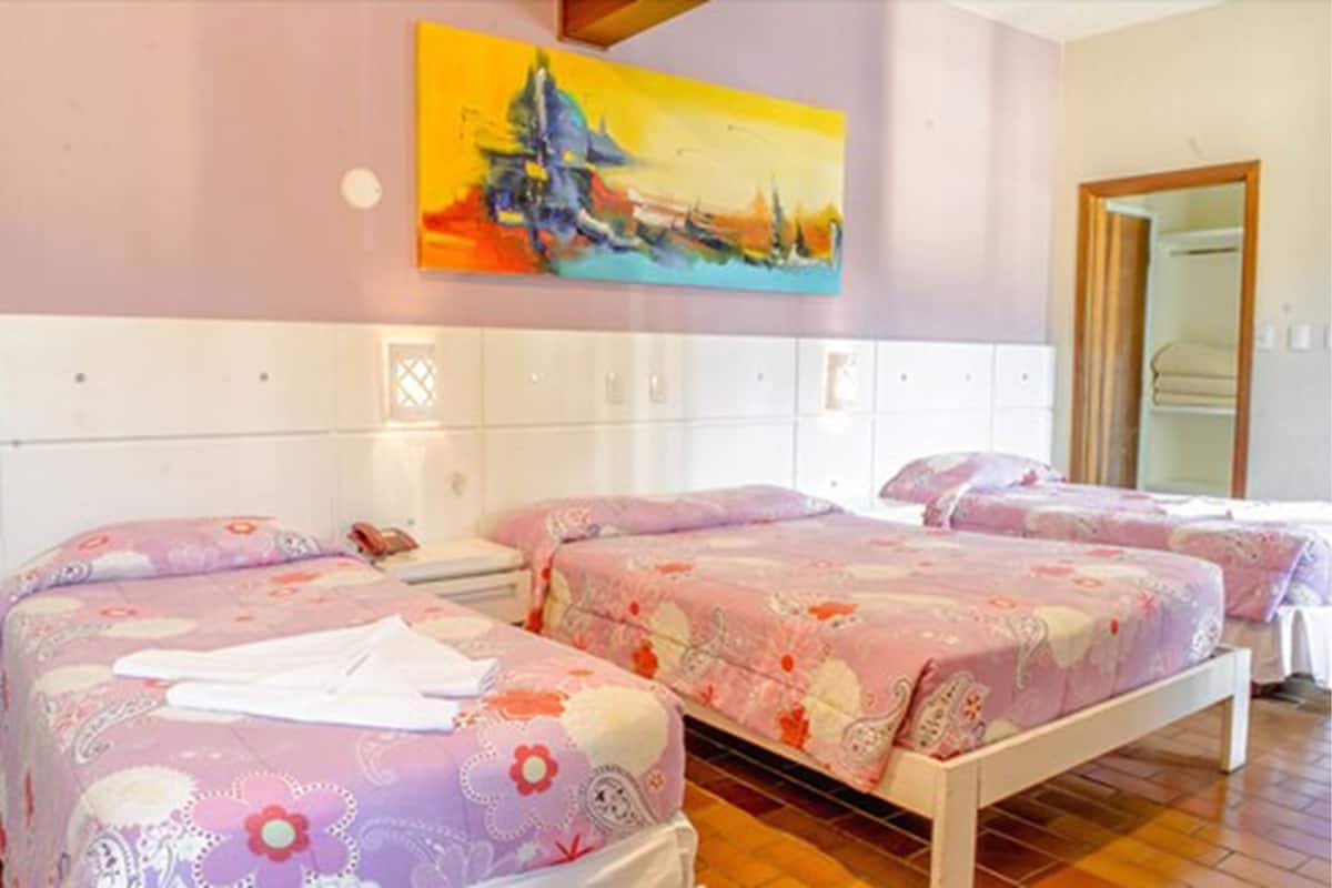 A hotel room with three beds, each with floral-patterned bedding, a large painting on the wall, and a wooden floor.