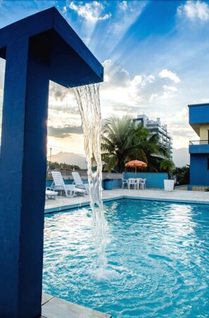 Una piscina con fuente, sillas de descanso y una palmera al fondo.