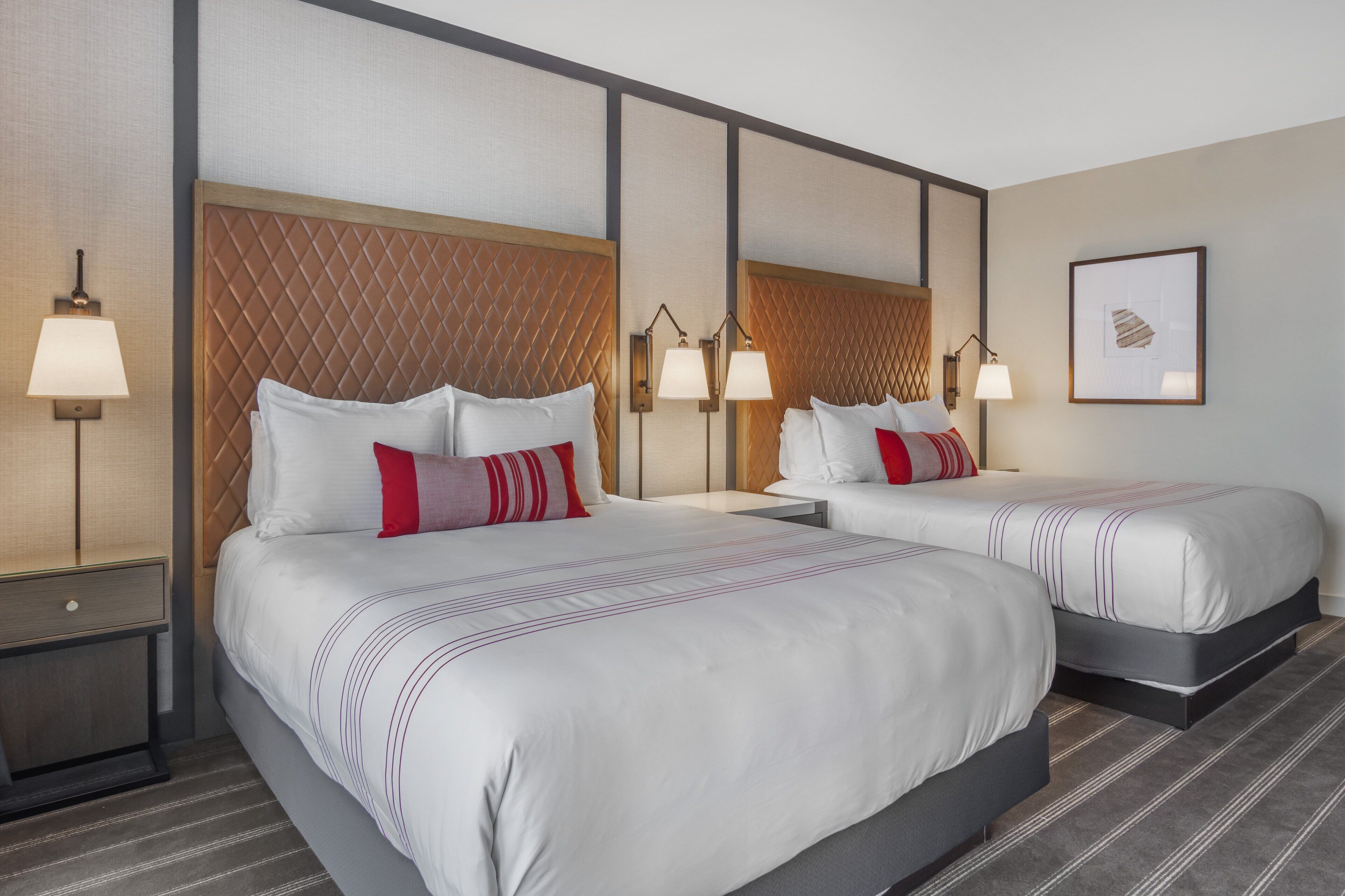 A hotel room with two beds, a nightstand, and a wall-mounted lamp.