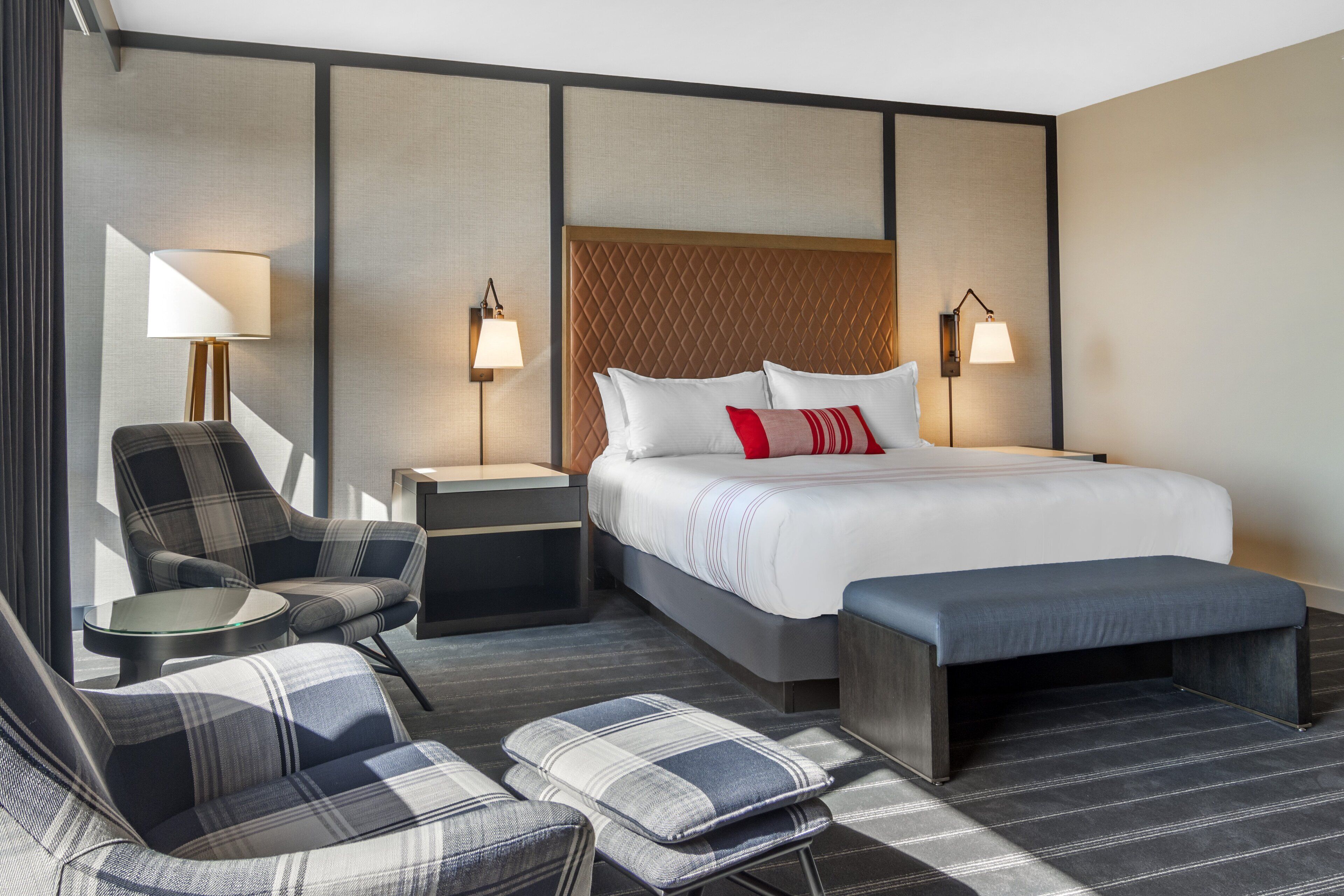 A hotel room with a large bed, two bedside tables with lamps, a sofa, and a bench.