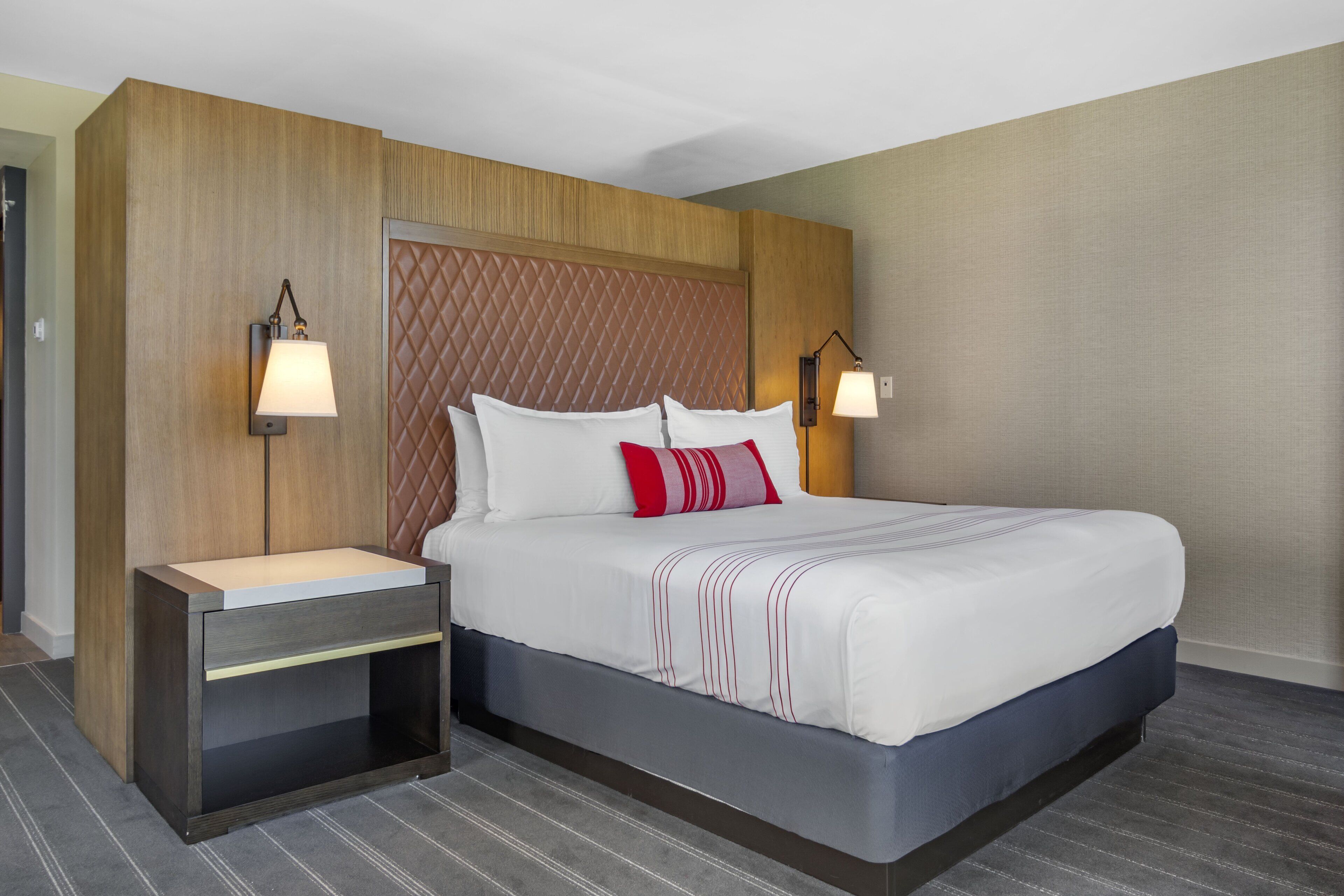 A hotel room with a large bed, a wooden headboard, two bedside tables with lamps, and a striped rug.
