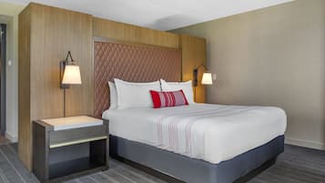 A hotel room with a large bed, a wooden headboard, two bedside tables with lamps, and a striped rug.