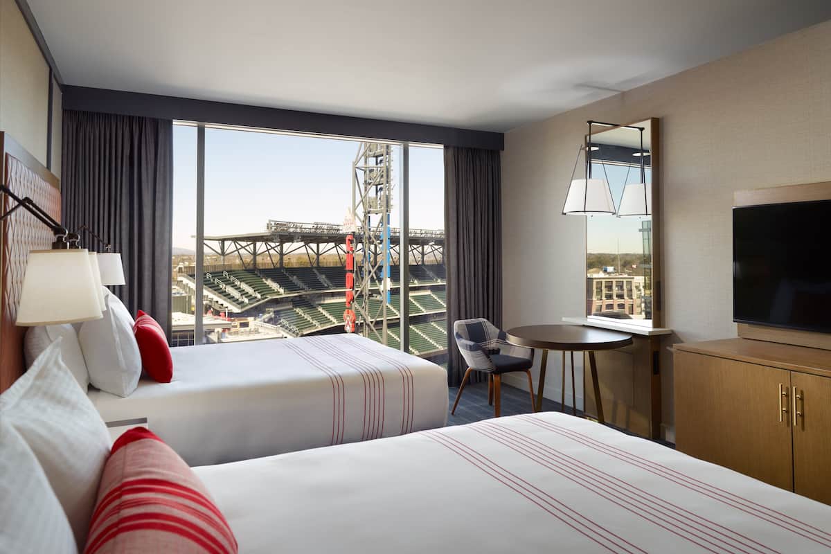 Une chambre d’hôtel avec deux lits, une télévision, un bureau et une vue sur un stade.